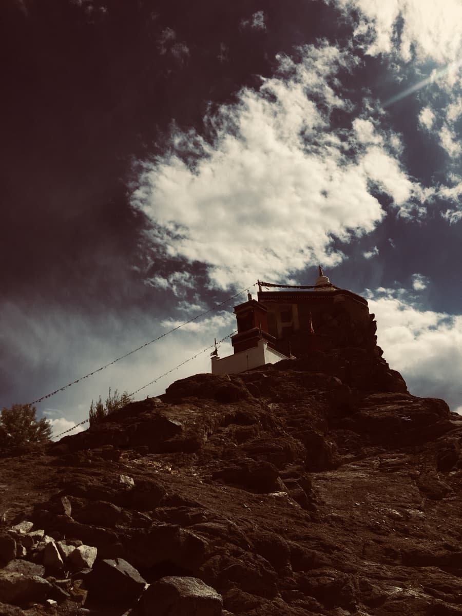 A small whitewashed stupa silhouetted against dramatic clouds on a rocky hilltop