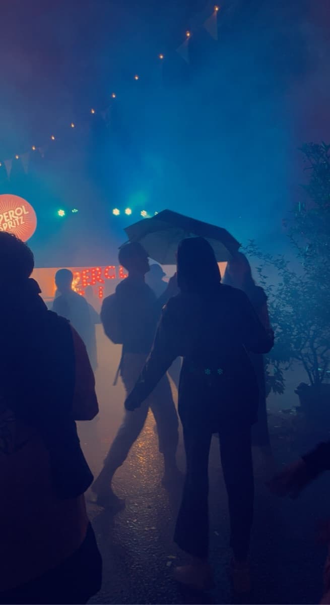 Silhouettes of people under bunting lights and thick blue haze at a night event