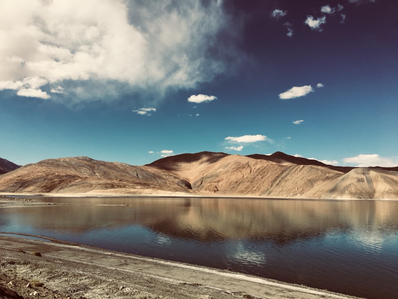 Still morning water beneath a ridgeline of sand-coloured mountains