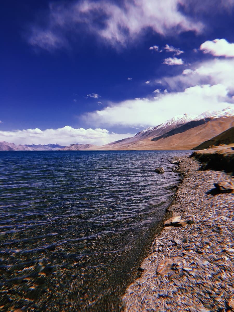 Pebbled shoreline of a deep blue high-altitude lake below snow-flecked peaks
